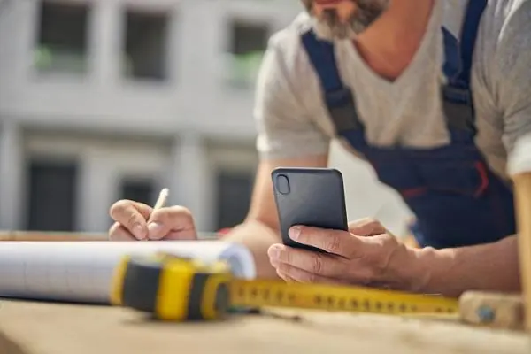 Contractor marking plans while holding a phone